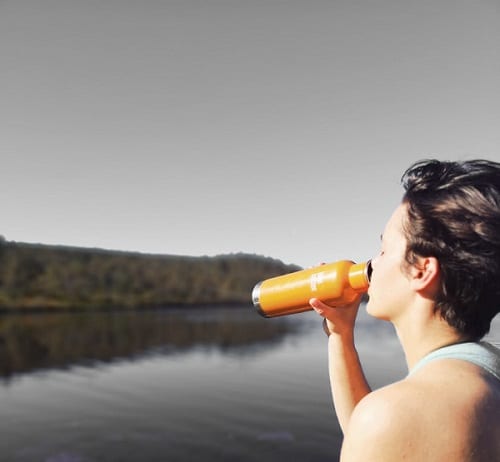 a woman drinks from an orange bottle when exercising outdoors