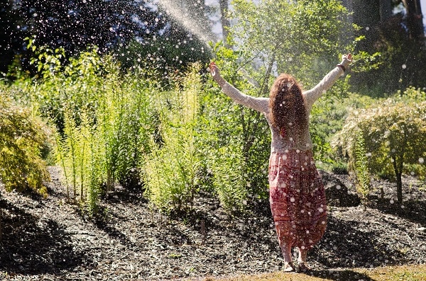 a woman enjoying water coming out a hose on a hot summer day