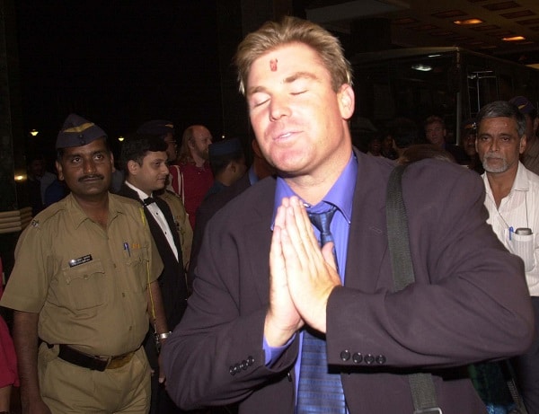 Australia's star spin bowler Shane Warne shuts his eyes and joins his hands in 'namaste', the traditional Indian style of greeting, as an Indian policeman looks on , on arrival in Bombay Wednesday Feb. 14, 2001. The Australian team starts an extensive cricket tour of India.(AP Photo/Sherwin Crasto)